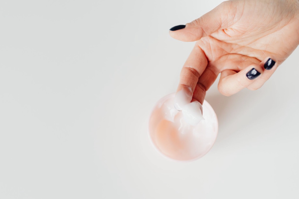 Manos con manicura impecable aplicando crema hidratante para la salud de las uñas.