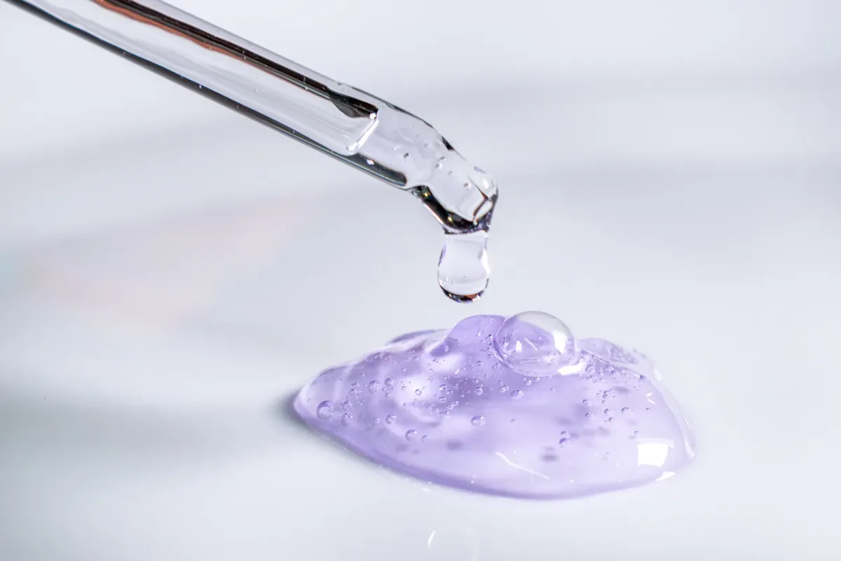 Pipette releasing drop of purple gel, highlighting skincare and laboratory use.