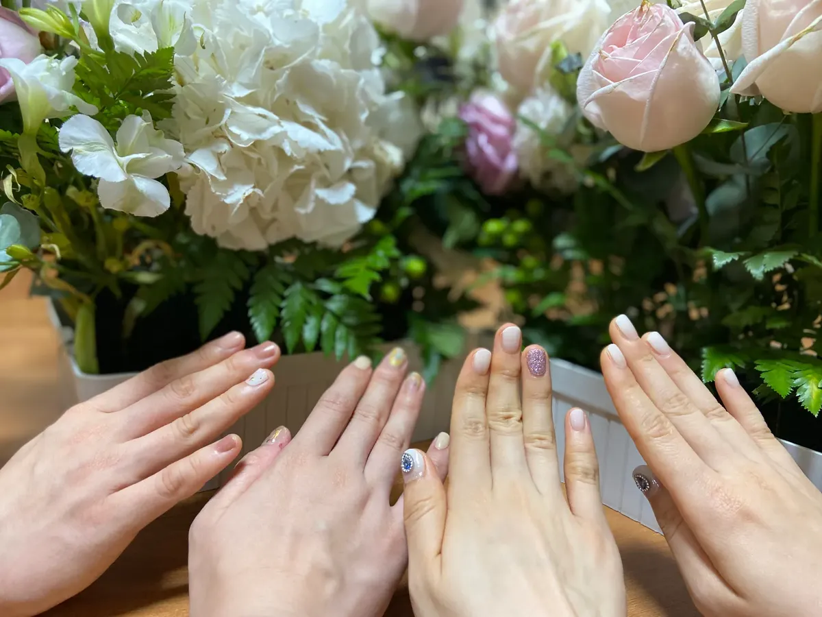 손의 그룹이 부드러운 꽃 조화로 둘러싸여 있고, 다양한 네일 아트를 보이는 사진입니다.