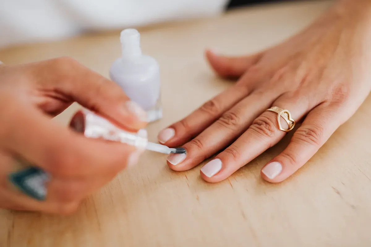 Detailed view of a hand receiving a manicure with nail polish application and a gold heart ring.